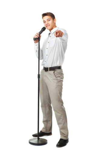 Young man singing into a microphone while pointing forward isolated on white background