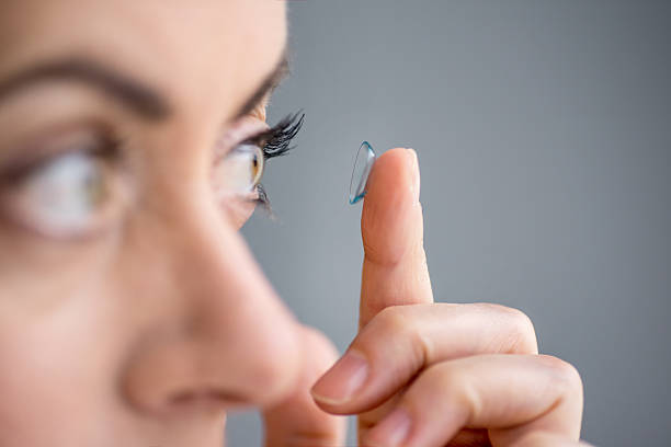 woman in her forties inserting contact lenses Attractive mature lady putting on contact lenses in her eyes contact lens photos stock pictures, royalty-free photos & images
