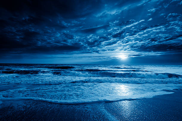 Midnight Blue Coastal Moonrise With Dramatic Sky and Rolling Waves stock photo