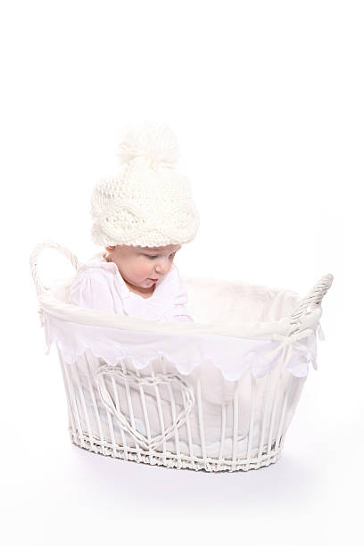 Baby girl in hat sitting in basket looking inside