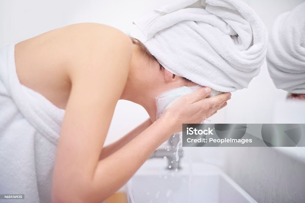 Final stages of her beauty treatment A young woman washing off her facial mask in her bathroom Soap Sud Stock Photo