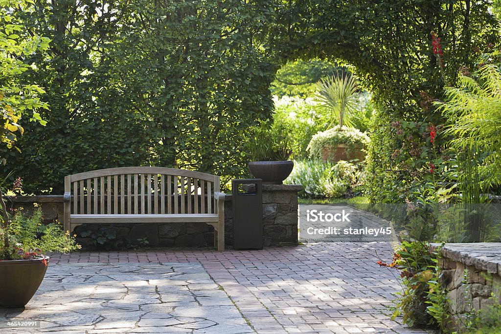 Arched Trellis in Lush Green Summer Garden Garden Furniture and Brick Pattern Walkway in a Public Courtyard and Sunlit Garden Yard - Grounds Stock Photo