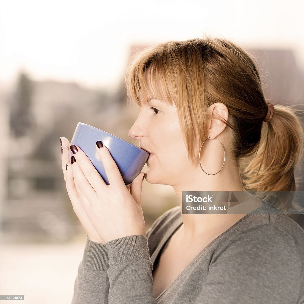 Morning view from the window Blonde woman looking through the window and drinking her morning tee. Adult Stock Photo