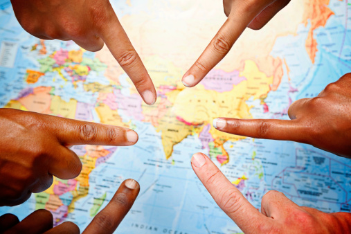Six  mixed hands point out India and the Indian sub-continent on a world map. Travel, politics, business, or geography could apply here.