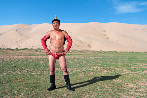 Mongolian wrestler standing on the grass, sand dunes on the background.http://bem.2be.pl/IS/mongolia_380.jpg