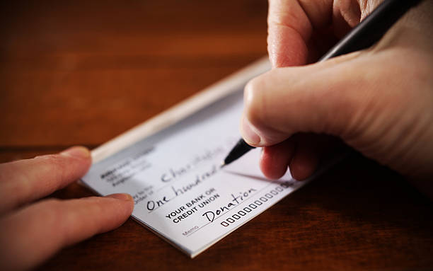 Close up View of Hand Writing A Donation Check Writing a donation check to a charitable organization charity and relief work stock pictures, royalty-free photos & images