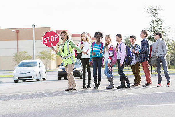 Children with school crossing guard School crossing guard (Hispanic mature woman, 50s) helping children walk across street. crossing sign stock pictures, royalty-free photos & images