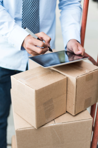 Business shipping and logistic theme. White-collar business man writing on tablet PC that is on top of boxes on a hand truck (dolly).