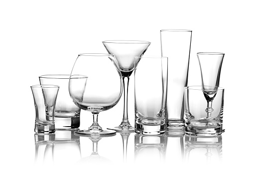 Collection of most common glasses used for alcoholic drinks isolated on white backdrop. This collection includes glasses for martini, scotch, liqueurs, cognac, beer and highball glass. Backlit and visible reflection of the glasses on foreground