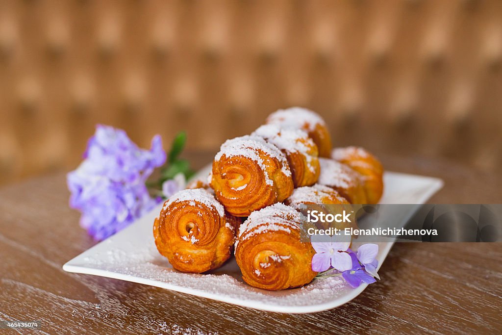 profiteroles with cream cream cake on a white plate which costs on a table, flowers lie nearby 2015 Stock Photo