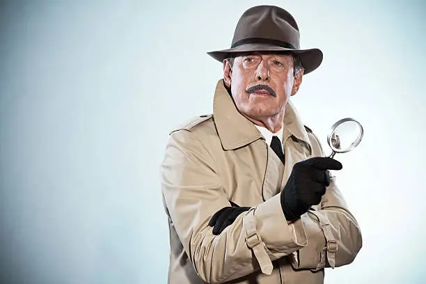 Retro detective man with mustache and hat. Holding magnifying glass. Studio shot.