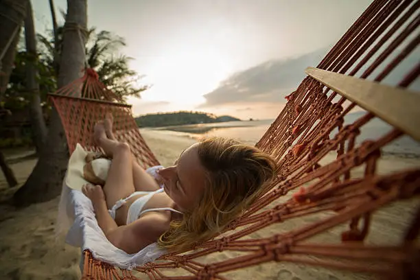 Young woman on a tropical beach in Thailand lying down on a hammock relaxing. Sunset time on the Island. Shot with 5D Mark III.