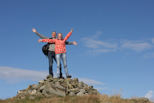 Walkers Standing On Pile Of Rocks With Arms Outstretched
