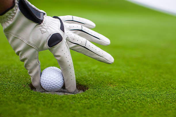 istock Man's hand putting golf ball into hole on green field 465447921