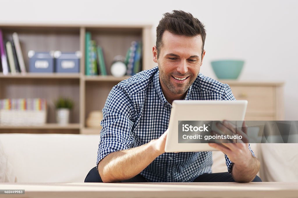 Smiling handsome man using digital tablet at home Smiling handsome man using digital tablet at home  Men Stock Photo