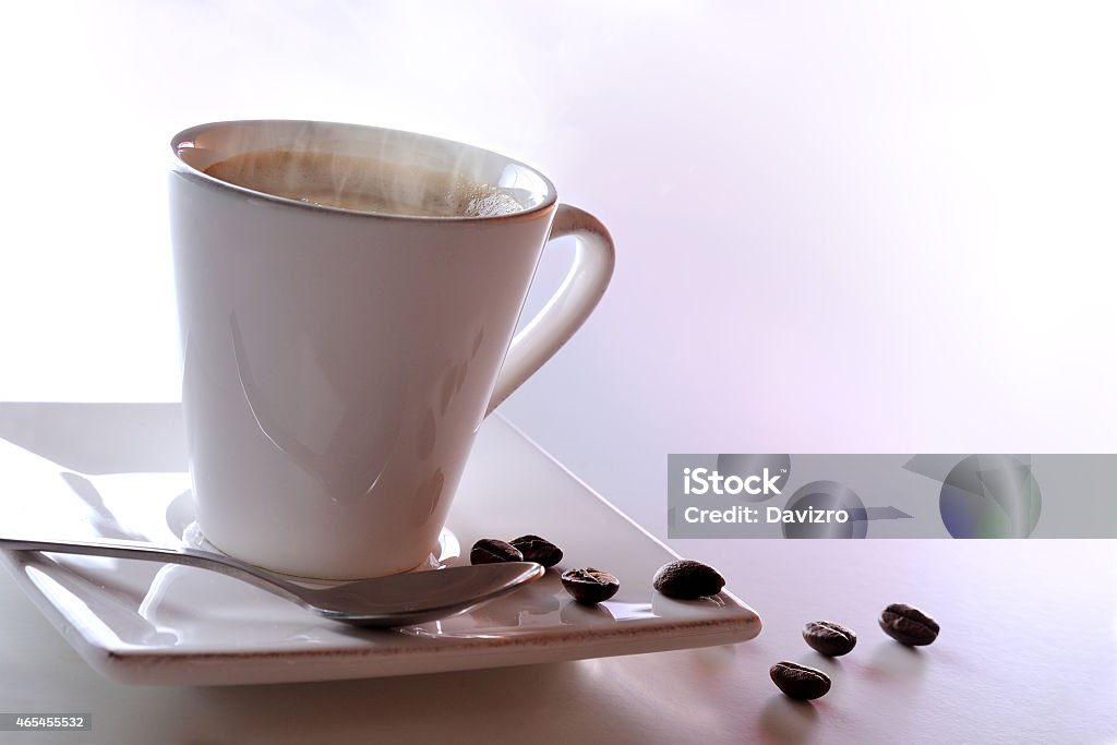 Steaming cup of coffee and beans Steaming cup of coffee and beans on a white table 2015 Stock Photo
