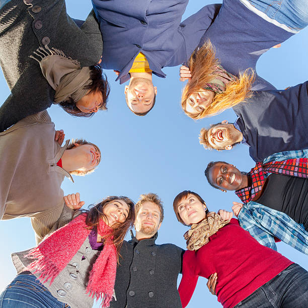 A diverse group forms a circle with hands stacked in the center, conveying teamwork, friendship, and mutual support. The scene highlights unity, collaboration, and shared purpose in a warm outdoor setting.