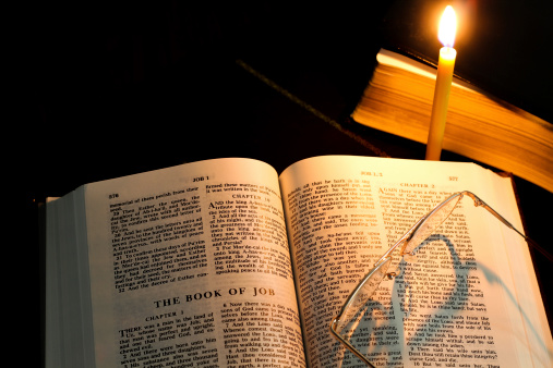 Read Bible The Book of Job under candlelight with glasses
