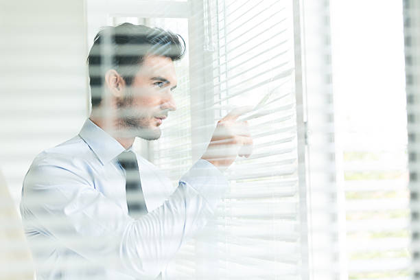 istock Businessman looking through closed blinds 465465036