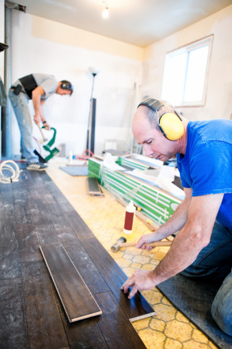 Two men installing hardwood floor during home renovations.