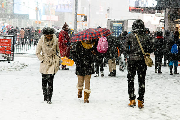 New York City, NY, USA - March 1, 2015: People head to their destination as snow falls in Times Square NYC. Lady with a plaid umbrella.  Snow coming down pretty fast and sticking on ground.