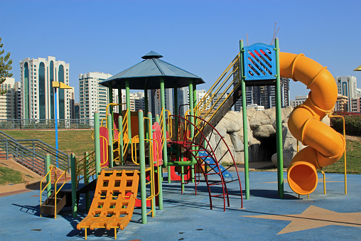 Inner city children's play area with colorful slides and climbing frame against a backdrop of a modern city