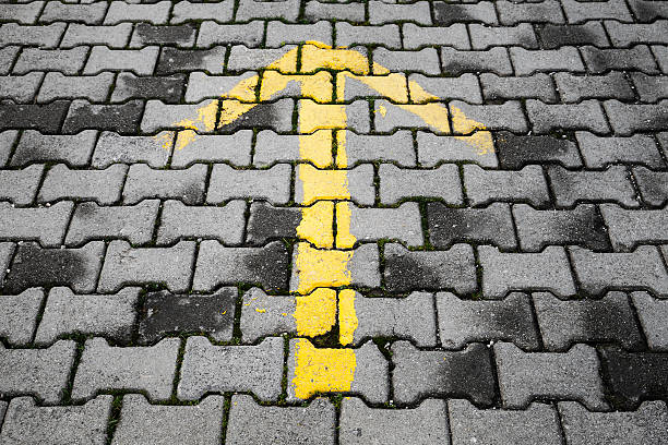istock Yellow arrow painted on dark gray cobblestone pavement 465472362