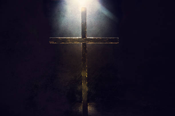 Dark Cross with Light Overhead A crucifix in a dark grunge setting is illuminated from above and behind by a bright and shining heavenly light.  Imagery intended to represent the crucifixion and resurrection of Jesus Christ celebrated on Easter sunday.  Horizontal image with copy space. religious cross stock pictures, royalty-free photos & images