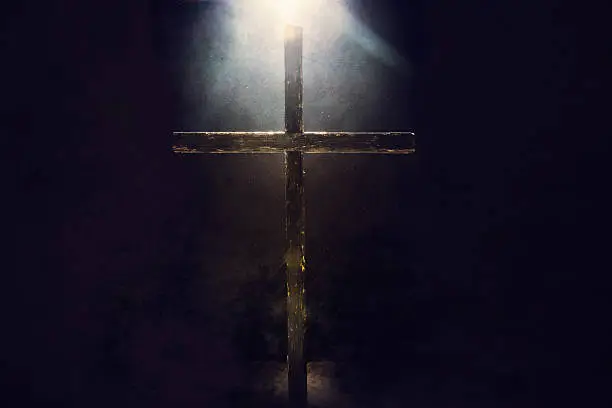 A crucifix in a dark grunge setting is illuminated from above and behind by a bright and shining heavenly light.  Imagery intended to represent the crucifixion and resurrection of Jesus Christ celebrated on Easter sunday.  Horizontal image with copy space.