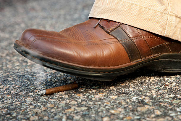 man's shoe sobre a passo sobre uma acesa beata de cigarro - round toe shoes imagens e fotografias de stock