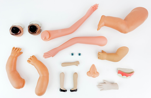 A collection of doll parts:legs, arms,eyes, nose, teeth. Horizontal.