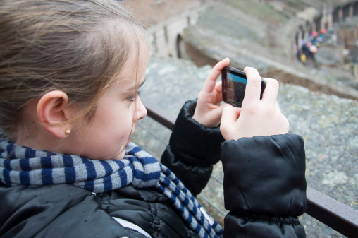 A nice little girl is taking a picture with a smartphone inside the roman ruins of the Coliseum. The Roman Coliseum, originally the Flavian Amphitheatre (in Italian Anfiteatro Flavio or Colosseo), is an amphitheatre in the center of the city of Rome, Italy, the largest ever built in the Roman Empire. It is one of the greatest works of Roman architecture and Roman engineering.
