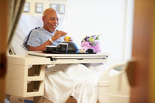 Senior Male Patient Enjoying Meal In Hospital Bed Senior Male Patient Enjoying Meal On Tray In Hospital Bed patience stock pictures, royalty-free photos & images