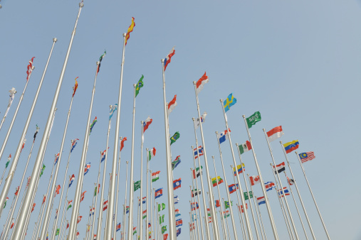 Rows of  flags of different nations fltutter on the pole against blue sky background.