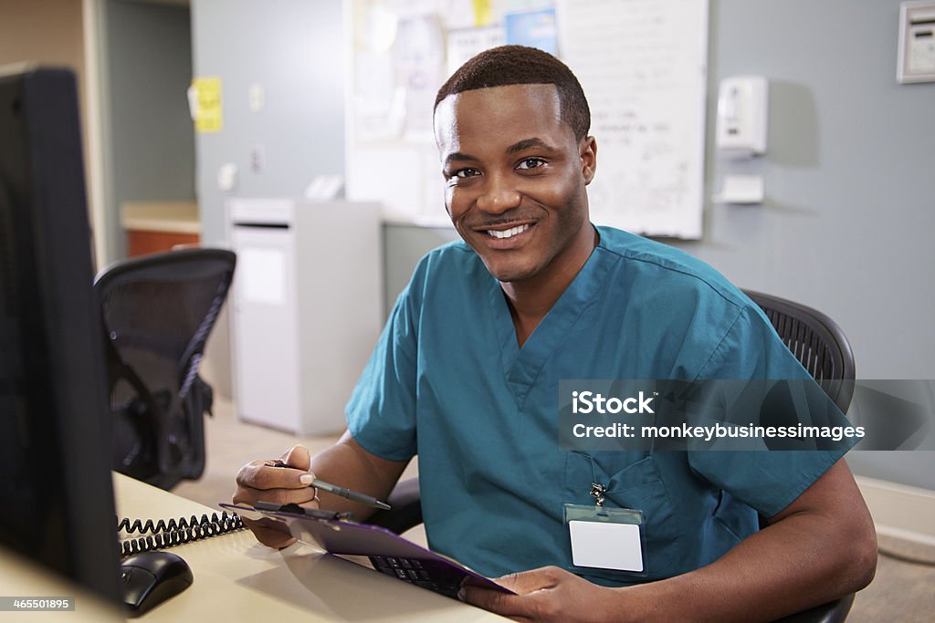 Portrait Of Male Nurse Working At Nurses Station Portrait Of Male Nurse Working At Nurses Station Smiling At Camera Male Nurse Stock Photo