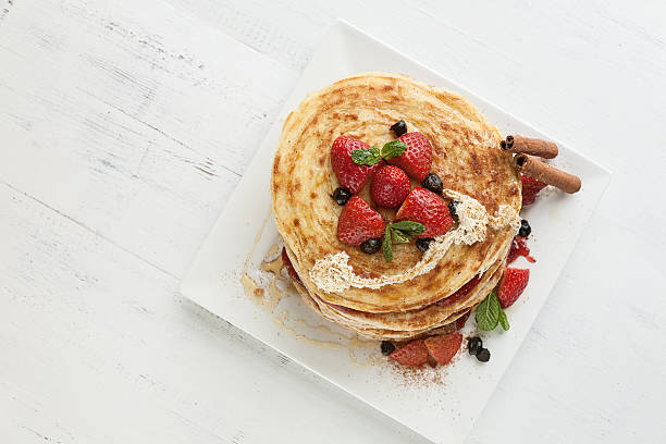 White plate full of pancakes with raspberries strawberries blueberries and honey on white wooden tableWhite plate full of pancakes with raspberries strawberries blueberries and honey on white wooden table