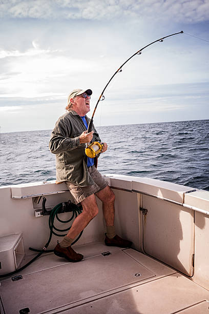 Man Fishing Mature adult male reeling in a fish on the ocean sea fishing stock pictures, royalty-free photos & images