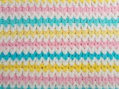 Hand-knitted pastel colored wool background in close up. There are white, yellow, pink and baby blue colored stripes at the pattern.