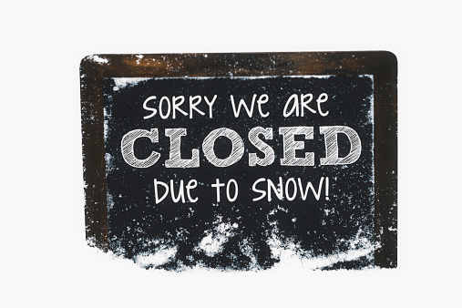 Snow-covered chalkboard reading Closed due to snow. Winter weather concepts.