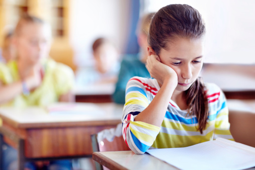 Depressed schoolgirl feeling excluded of her friend during a break in the classroom. Her friends are in blurred motion.