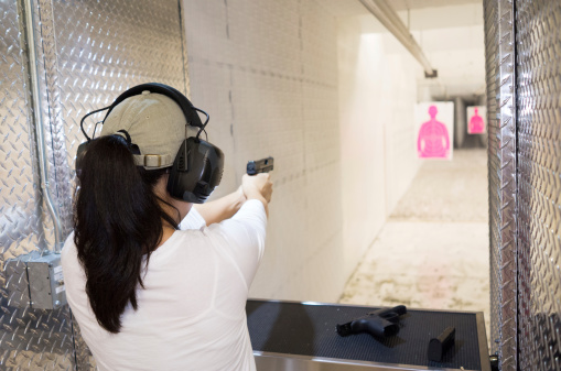 Young woman aiming handgun down range at gun club.