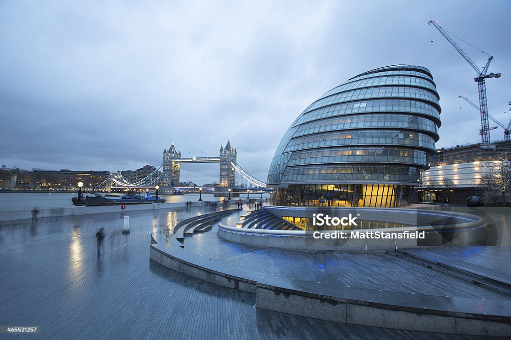 City Hall and London Bridge A moody, London evening scene showing City Hall with London Tower bridge in the background. Both popular landmarks for tourists and visitors to the city. You can also see the steps in the foreground for theScoop at More London, which is an outdoor sunken amphitheatre with seating for 800. Throughout the summer months it regularly hosts a variety of free events. London - England Stock Photo