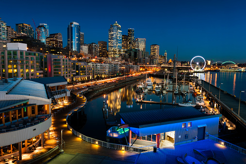 The Seattle, Washington waterfront and skyline at sunset with a marina and ferris wheel. The Port of Seattle can be seen in the background.