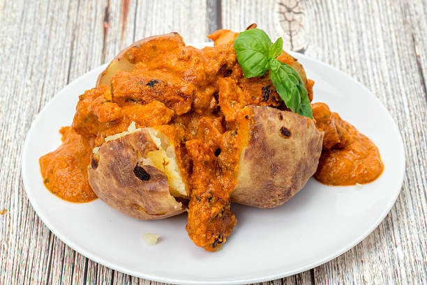 A baked potato filled with spicy Chicken Tikka Masala curry - studio shot