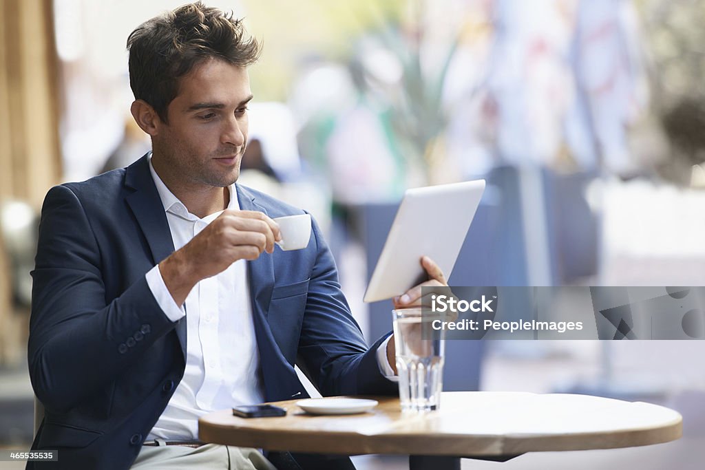 Catching up online with an expresso Shot of a young businessman sitting at an outdoor cafe using a digital tablet E-Reader Stock Photo