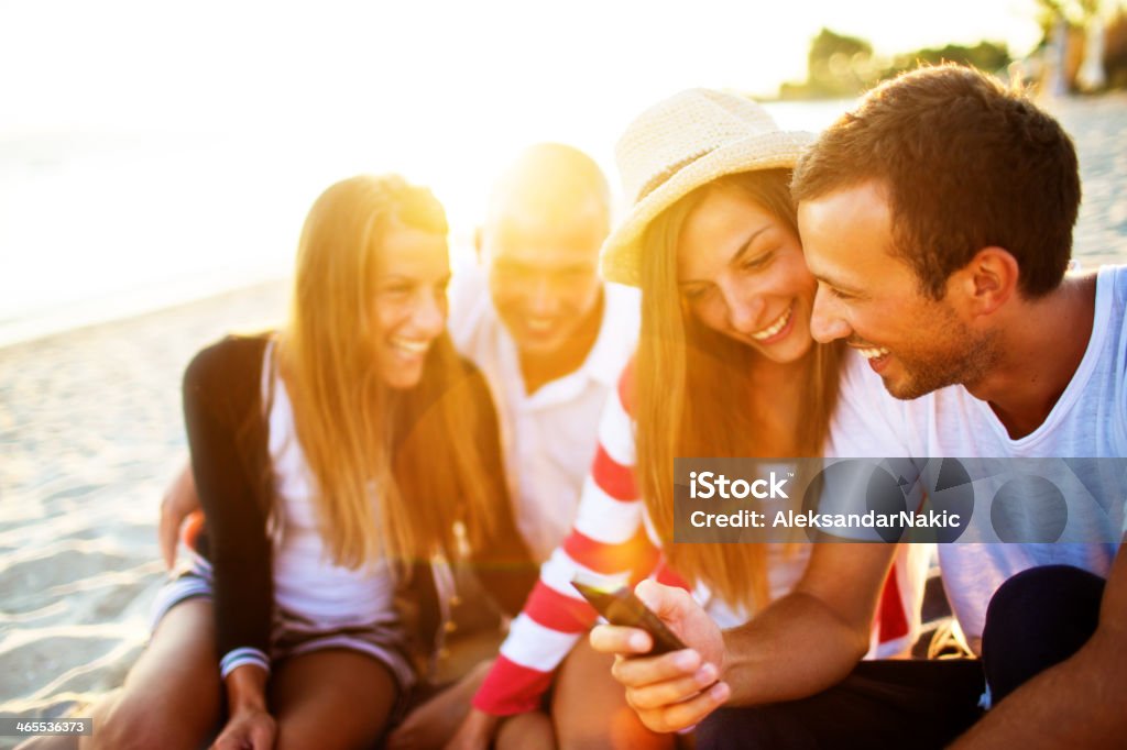 Freunde sitzen auf einem Strand-Lächeln und mit Telefon - Lizenzfrei Strandparty Stock-Foto