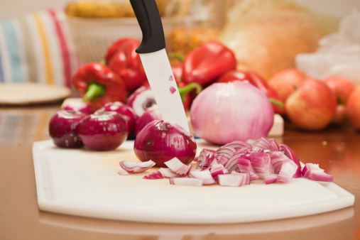 Red onions chopped with ceramic-blade kitchen knife on plastic chopping board; selective focus;