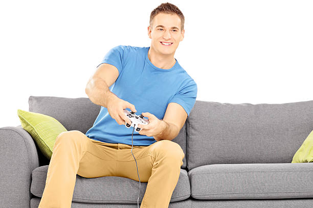 istock Young smiling man seated on a couch playing video game 465538483