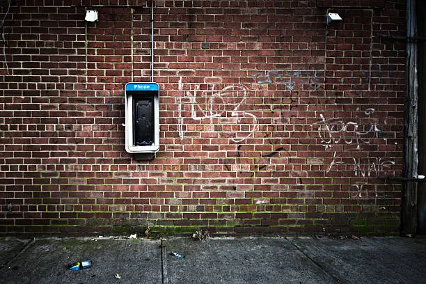 Grungy urban background of a brick wall with an old out of service payphone on it