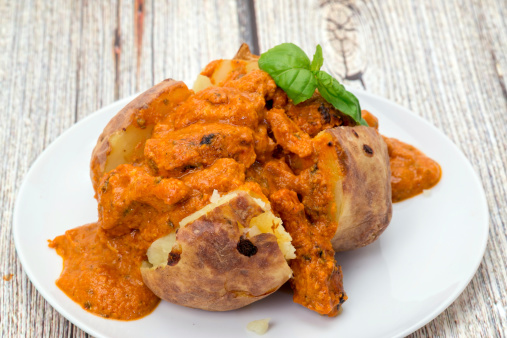 A baked potato filled with spicy Chicken Tikka Masala curry - studio shot
